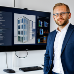 Brandschutzexperte im Büro**

"A professional male Brandschutzexperte (fire protection expert) in his late 30s, fully clothed in a modern business suit, standing in a bright, modern office in Germany. Behind him is a large screen displaying BIM (Building Information Modeling) software with a building plan. The office has a clean, minimalist design. Safe for work, appropriate content, perfect anatomy, natural proportions, professional, modest, high quality."

**